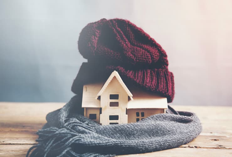 A wooden house wearing a beanie hat and scarf. Image represents energy efficiency and heating.