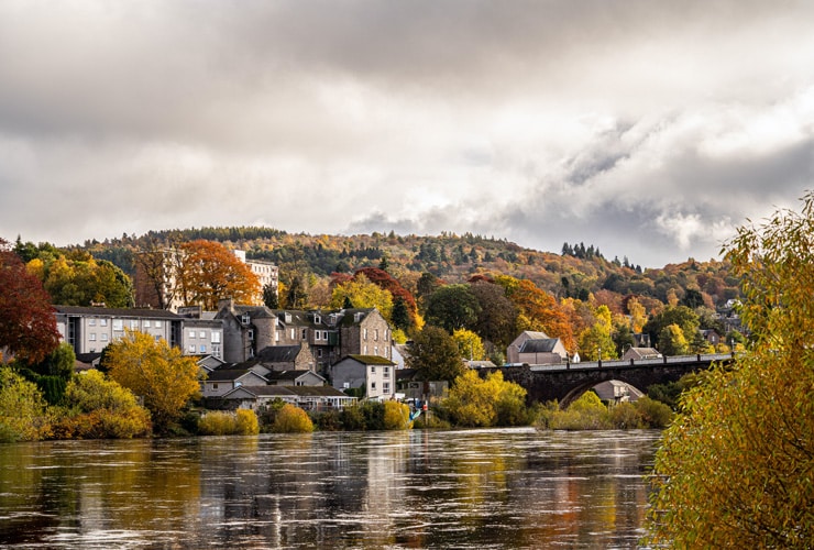 An autumnal scene of Perth in Scotland, the city seen among red, yellow and orange trees