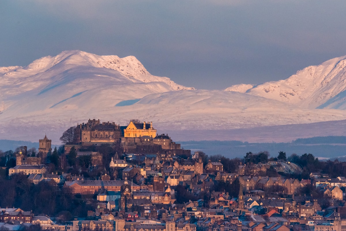 Stirling Castle in winter, sitting on a hill with snowy mountains behind