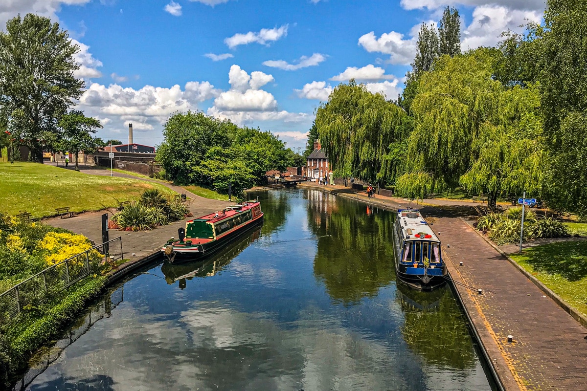 View of the Wolverhampton canal walk-way with a blue sky reflected in the water and longboats moored at the edges