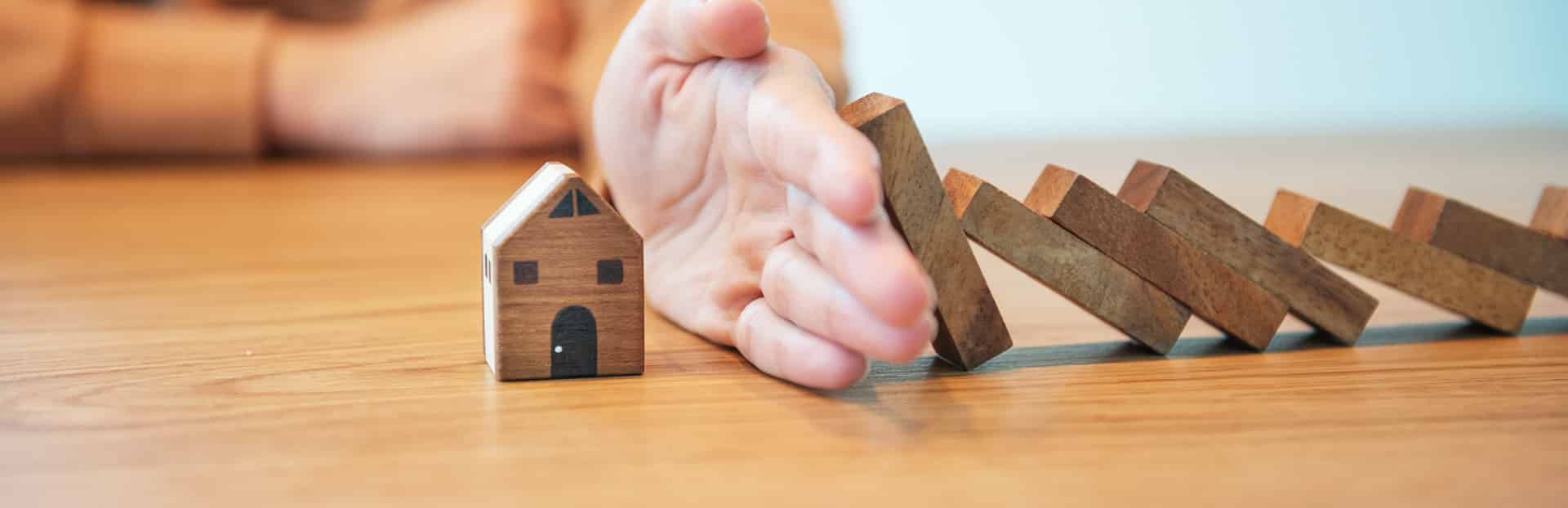 Block Repossession, Concept Blocks falling onto a toy house are blocked by a hand. Represents stopping a repossession.