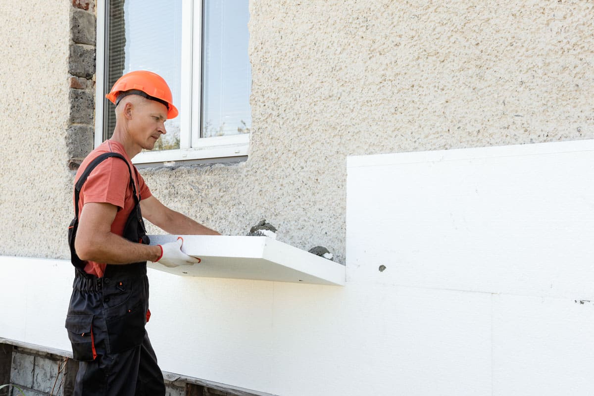 A worker installing a styrofoam board on the facade of a house.